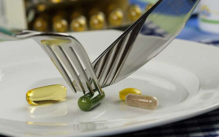 Vitamin supplements on a plate, being cut by a fork and knife.