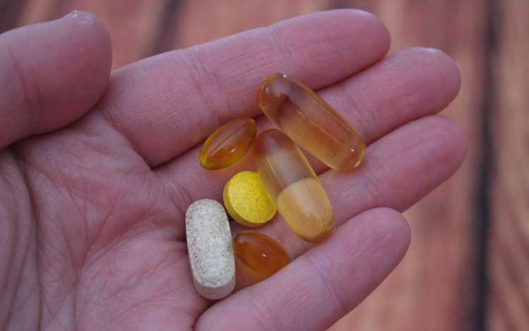 Vitamin supplements in a person's hand, in capsule and tablet form.
