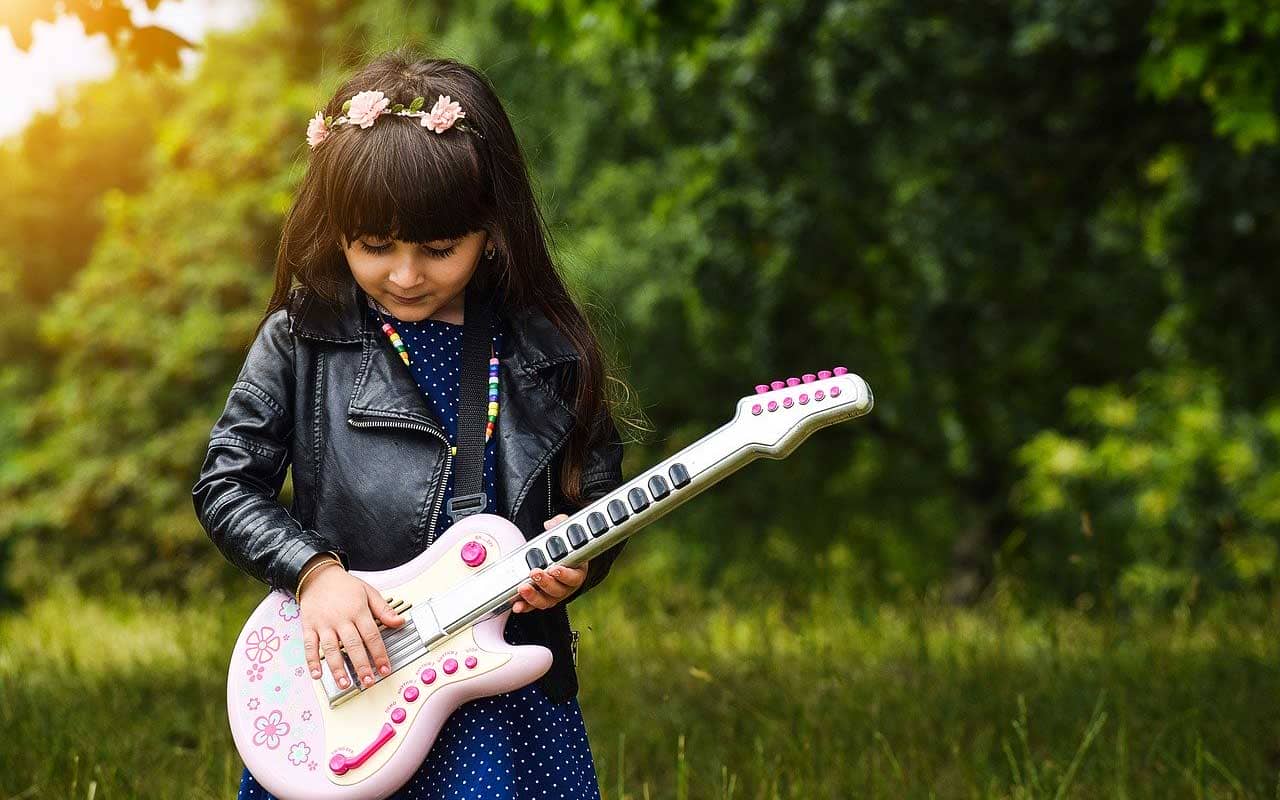 A girl with a leather jacket and flowers in her hair plays a pink plastic guitar.