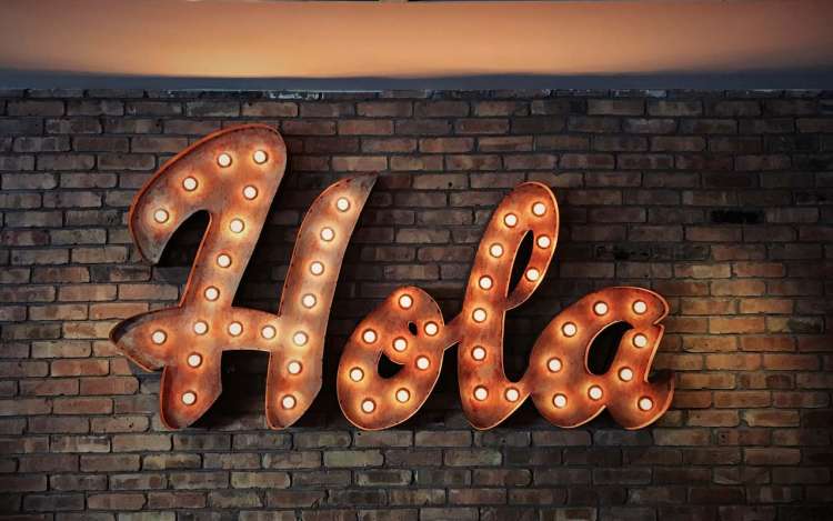 An illuminated sign says "hola" against a brick wall.