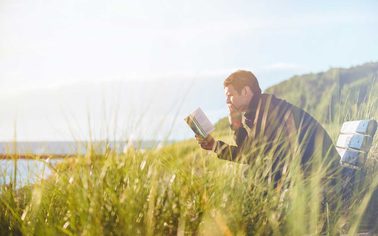 A man reads a book on a bench outside. He appears to be fully focused, in a flow state.