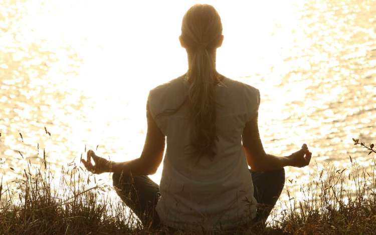 A woman sitting by a lake practicing mindfulness meditation.