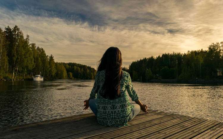 A woman meditating at the lake, practicing mindfulness.