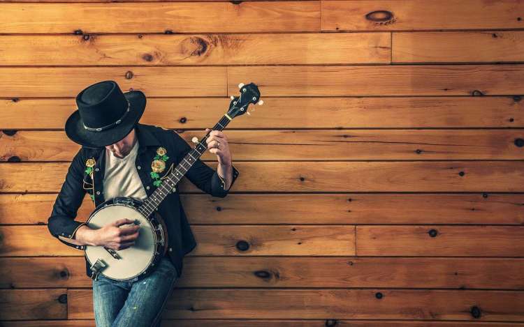 A musician with a banjo leaning against a wooden wall, learning how to memorize song lyrics.