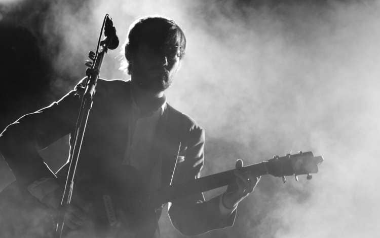 A man plays the guitar at a microphone in a cloud of smoke.