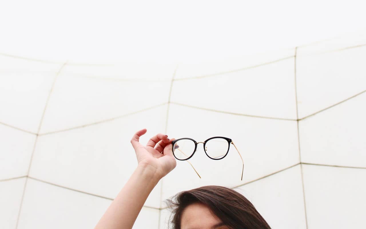 A woman holds a pair of reading glasses above her head. Forgetting what reading glasses are for would be an indicator that memory disorders might be to blame.