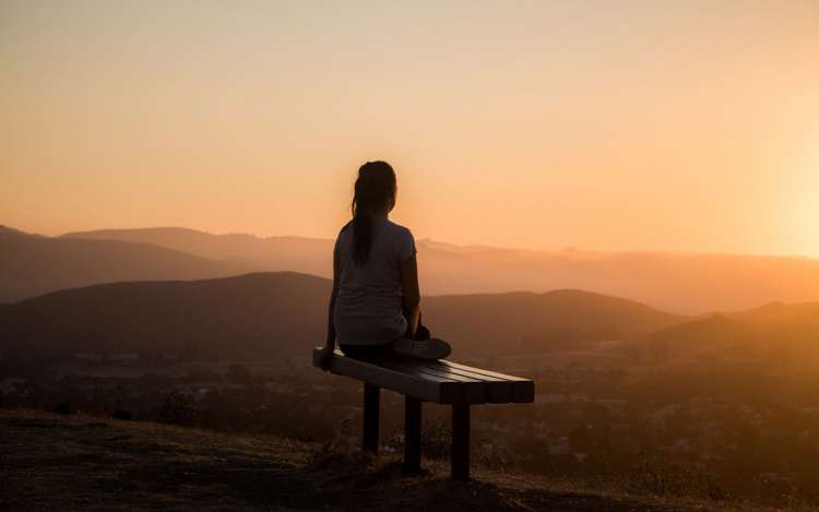 A woman on a bench overlooking a sunrise, using concentration meditation to help her focus on work.