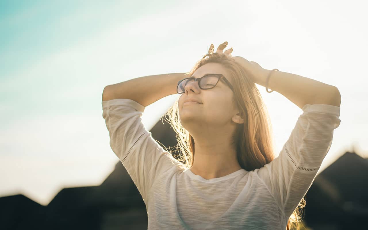 A woman turns her face to the sky with a big relaxed smile on her face.