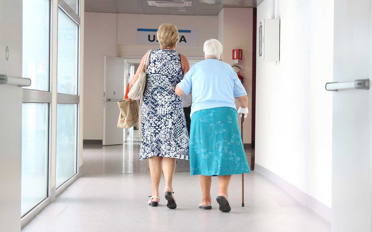A woman walks her elderly mother through a medical facility. Early diagnosis of memory disorders can help caregivers and patients cope with their disease.