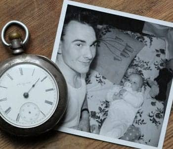 A black and white photo of a man and a baby, with a pocket-watch sitting beside the photo.