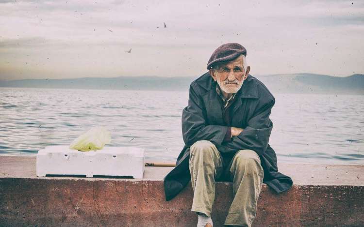 An old man sits on a sea-wall.