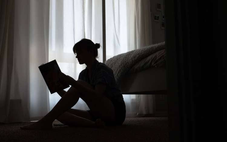 A woman in silhouette, reading a book. Reading is one of many cognitive activities for adults.