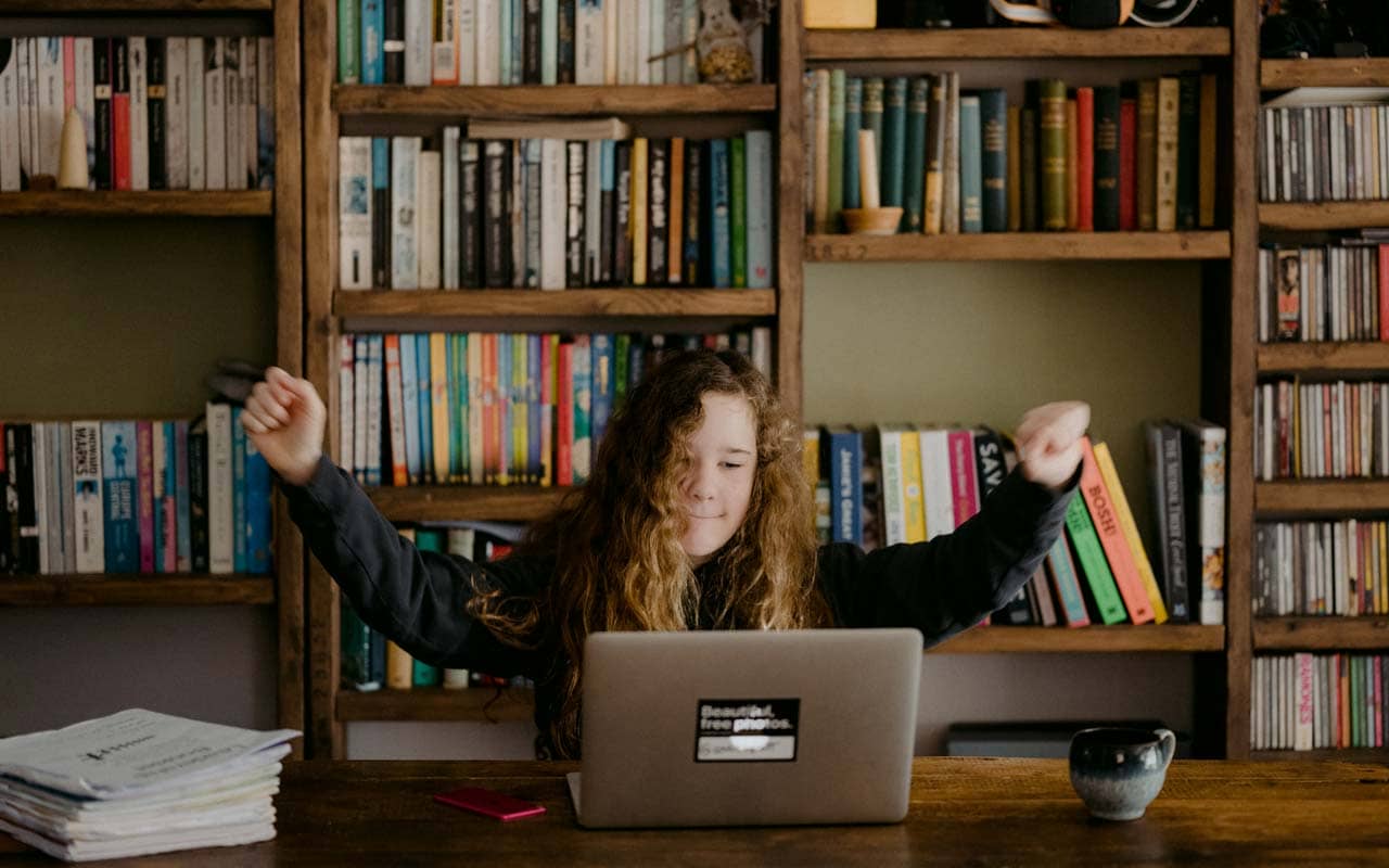 A young woman learns memory techniques at her laptop in front of a bookshelf.