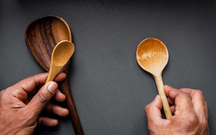 A person holds wooden spoons in their hands, spaced apart on a table.