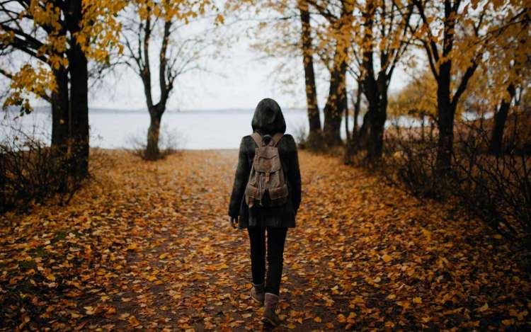 A person walks along a leaf-covered road. Mindful walking like this can be a good cognitive activity for adults.