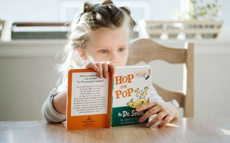 A young girl reads the book Hop on Pop by Dr Seuss, aiding her cognitive function development. 