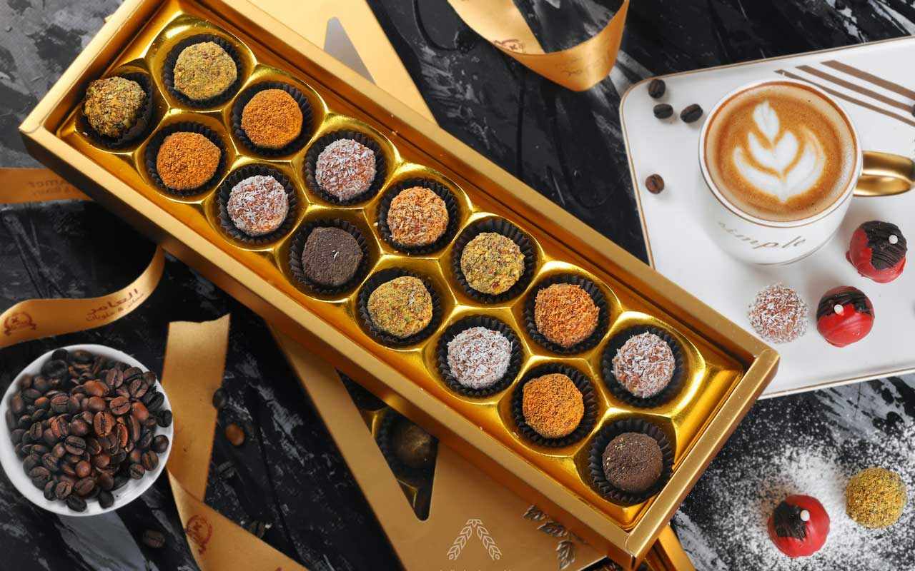 A tray of chocolates sits next to a cup of coffee beans and a cup of coffee. Chocolate and coffee are both known to improve concentration.