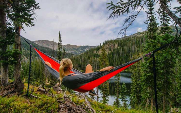 A woman relaxes in a hammock above a wilderness lake. Imagining yourself relaxing in a hammock is one type of visualization for relaxation.