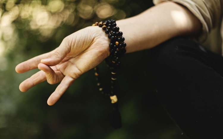 A person wearing mala beads around their wrist makes a mudra (hand gesture) while meditating.