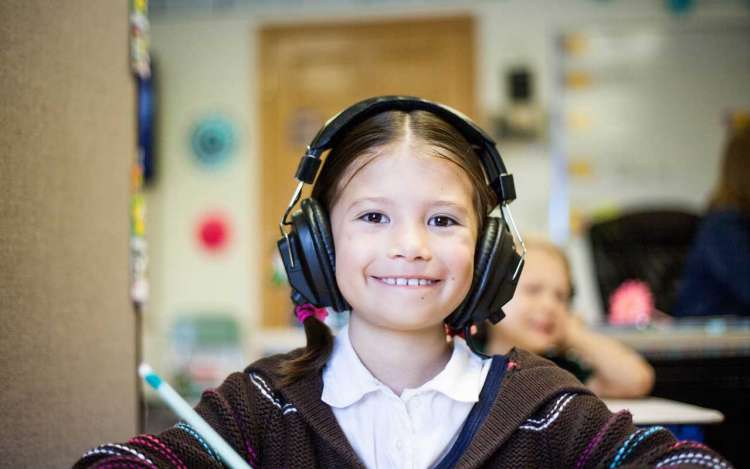 A young girl with headphones on smiles at the camera.