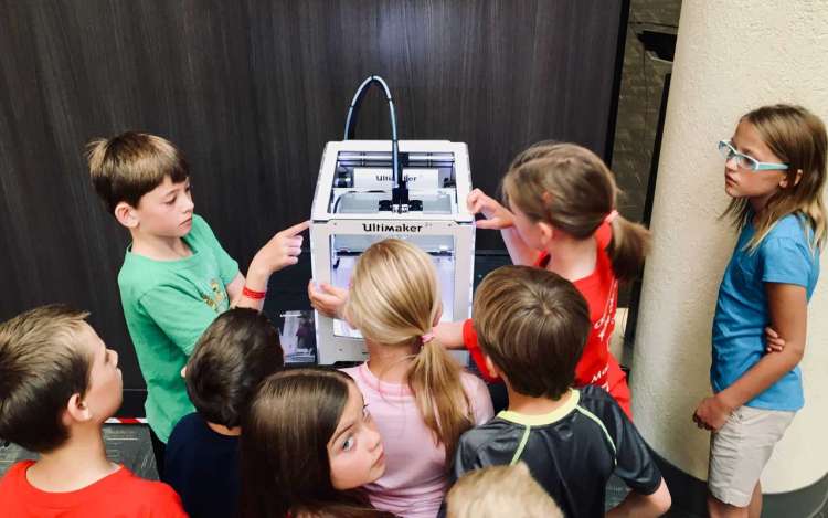 Students gather around a 3D printer, an example of creative problem-solving.