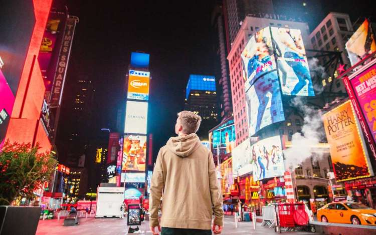 A young person stands in the middle of Times Square in New York City, surrounded by advertisements. Eliminating ads from your life can help you improve concentration.