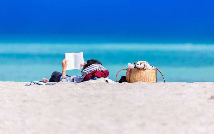 A person relaxes on the beach with a book, possibly helping them visualize while reading.