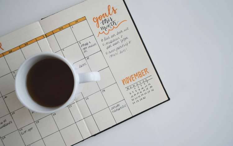 A cup of coffee sits on a monthly goals calendar. Keeping achievable goals can help you learn how to stay focused while studying.
