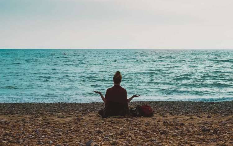 A woman meditates by the ocean. Meditation can help you concentrate on studies by clearing your mind ahead of time.