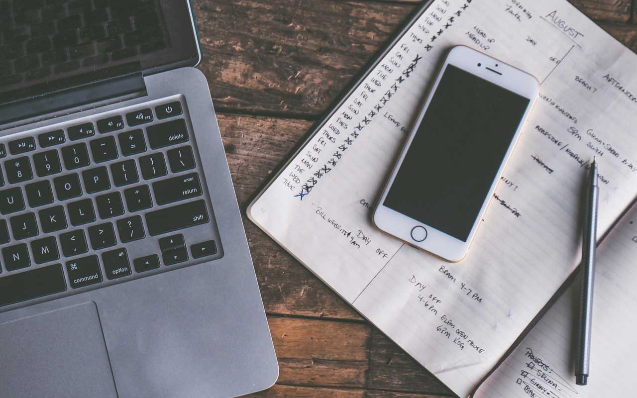 A phone sits on top of a study planner on a table beside a laptop. Keeping a rigorous study schedule will help you focus on studying.