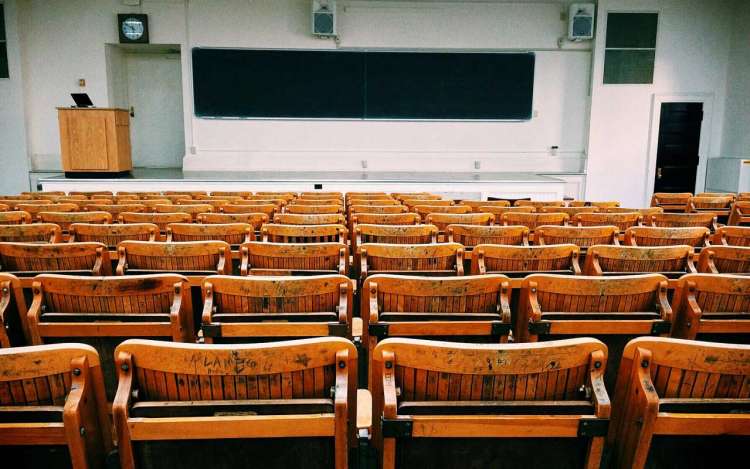 An empty college lecture hall with wooden chairs and a blackboard.