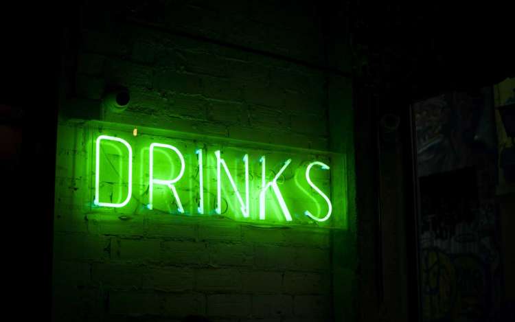 A green neon sign says DRINKS. Alcohol consumption can impair memory in adults.