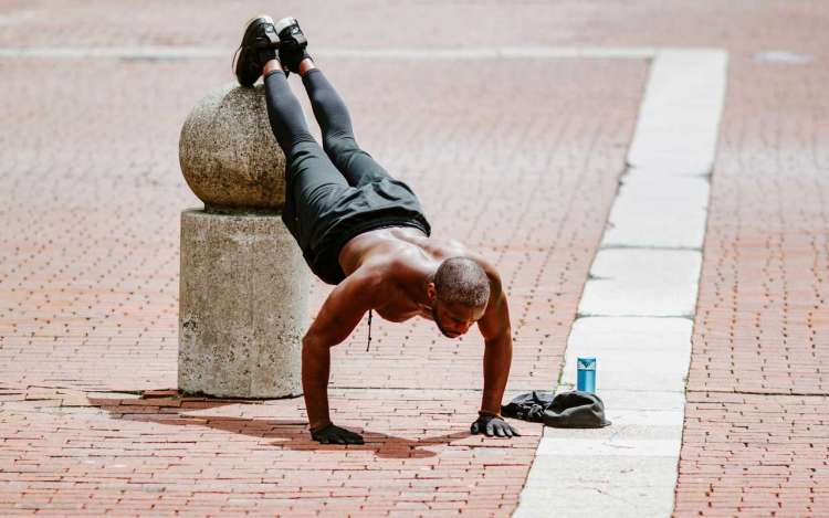 A man does pushups in an outdoor square, with his feet elevated on a concrete pier. Exercise is a natural memory enhancer.