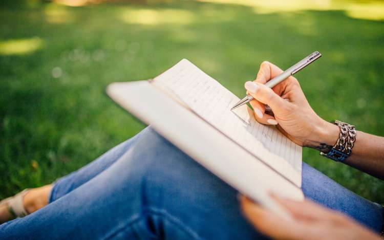 A person writes in a journal while sitting in the grass. Practices like journaling helps you gain focus.
