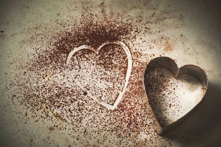 A heart-shaped cookie cutter sitting beside the outline of a heart in cocoa powder.