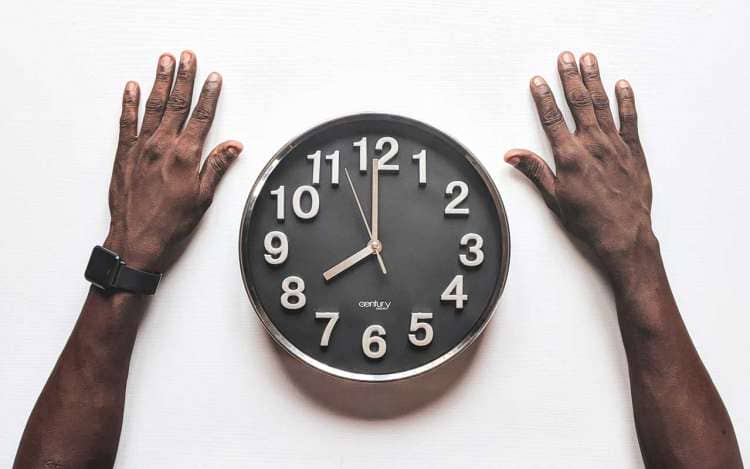 A Black man's hands next to an analog clock. 