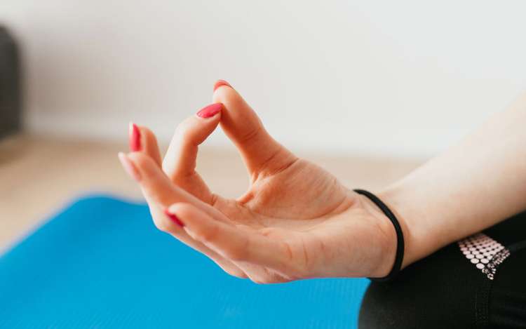 A woman's hand with red fingernails, in a yoga mudra. Meditation for mindfulness and concentration provides cognitive benefits.