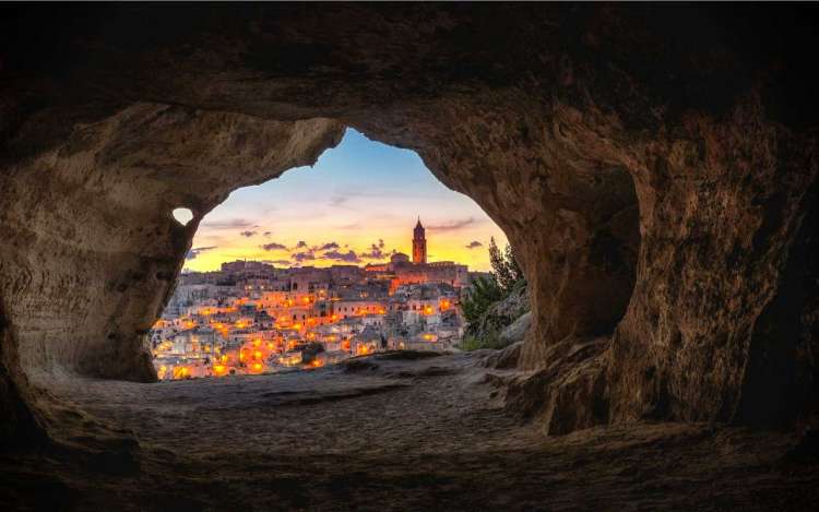 The mouth of a cave looks out over a city at dusk. 