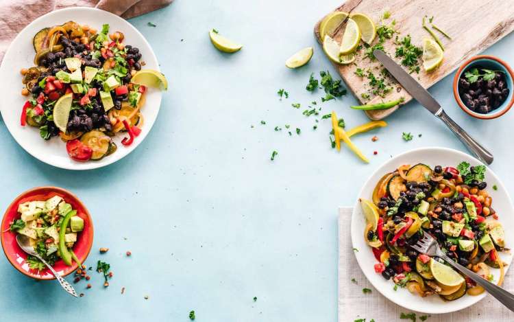 Salad bowls and a cutting board with limes sit on a blue tablecloth. Healthy foods like fruits and vegetables are natural memory enhancers.