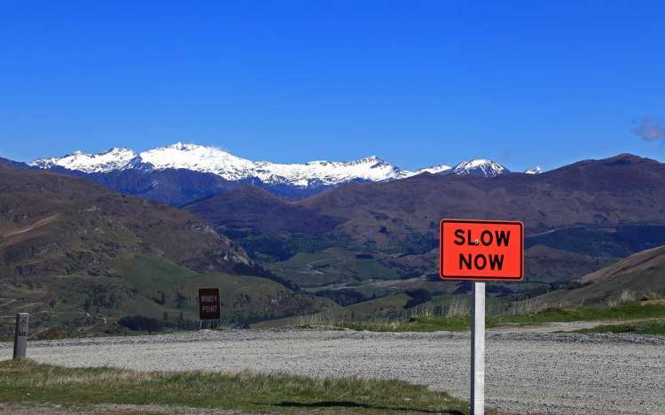 A sign saying "slow now" in front of a mountain backdrop with a clear blue sky.
