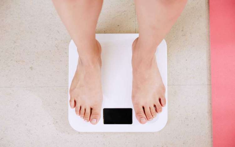A person stands on a scale. Maintaining a healthy weight is one way to improve memory.