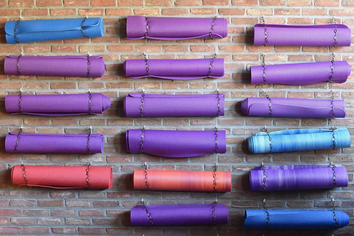 Yoga mats in multiple colors (purple, blue, and red) hang horizontally against a brick wall.
