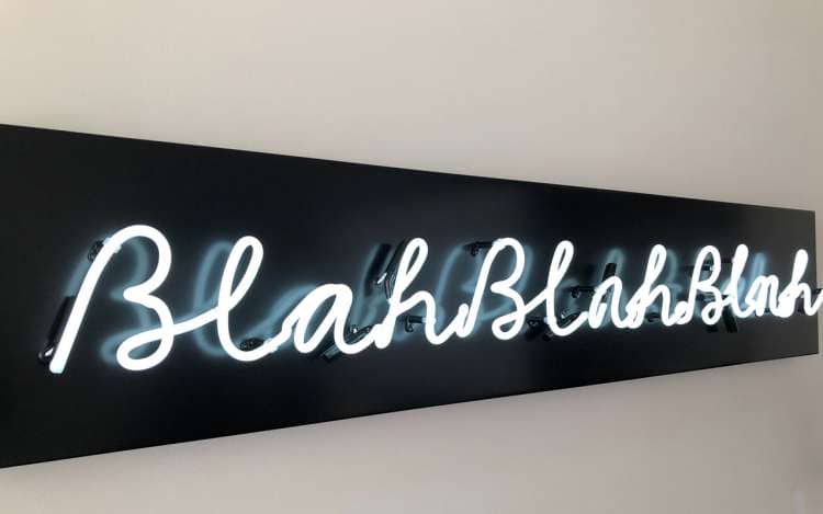 A neon sign with white letters against a black background reads "blahblahblah."