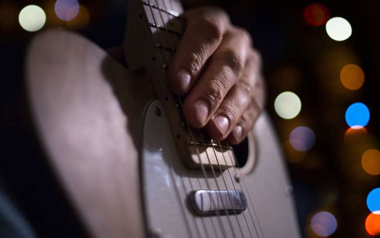 A person's hand sits on the frets of a guitar.
