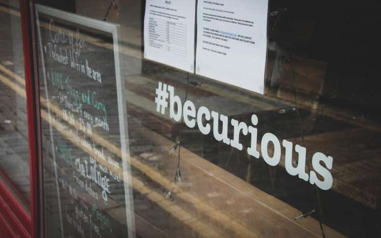 A graphic in a restaurant window reads "#becurious"