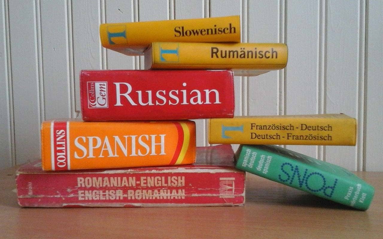 A stack of Russian, Spanish, Romanian, and German dictionaries sit on a desk.