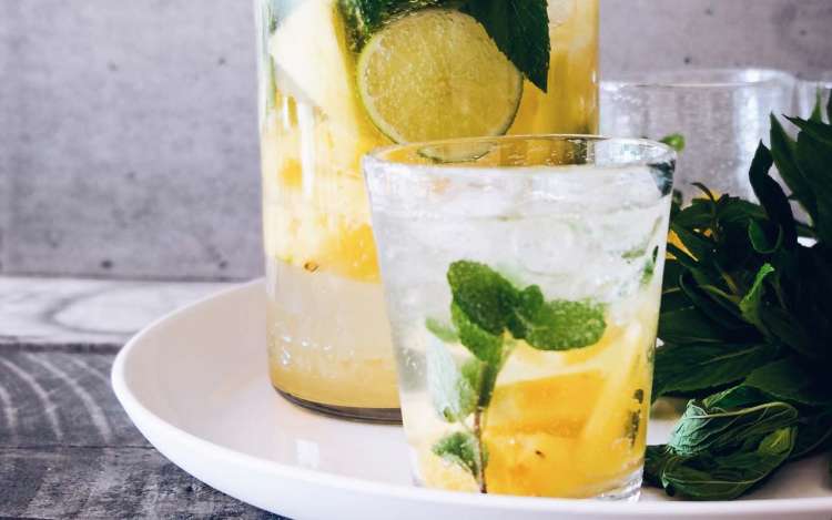 A glass of water with slices of lime, pineapple, and mint.