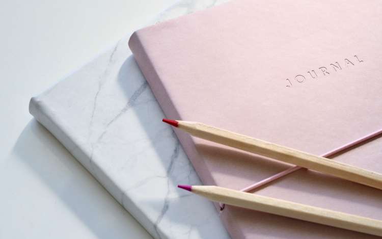 Two journals sit against a blank surface, with 2 colored pencils on top. Journaling can help you learn how to visualize effectively.