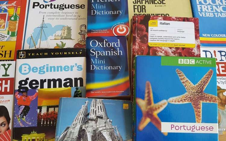 A stack of language learning books spread out on a table. Learning how to speak fluently can be overwhelming if you use too many materials.