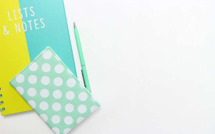 A yellow and blue notebook with "Lists & Notes" lettered on the cover, as well as a sea-foam green journal and pen.